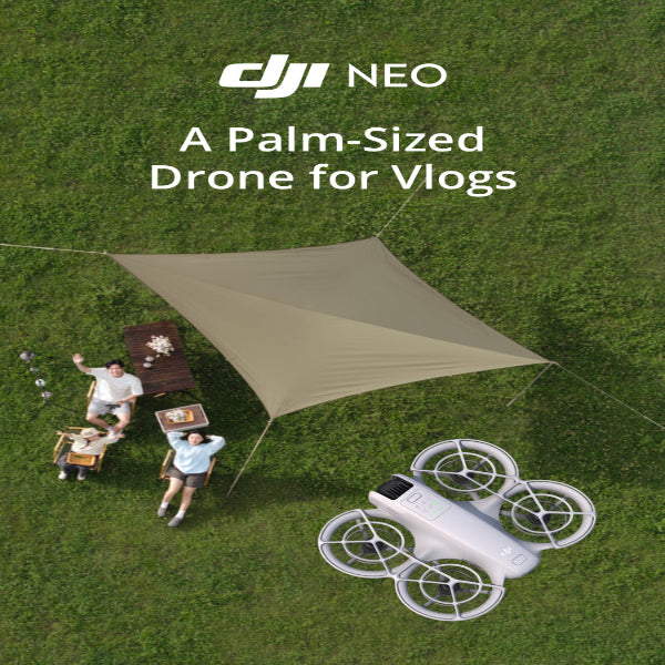 DJI Neo 4K Camera Drone in white flying over grass near people enjoying a picnic outdoors