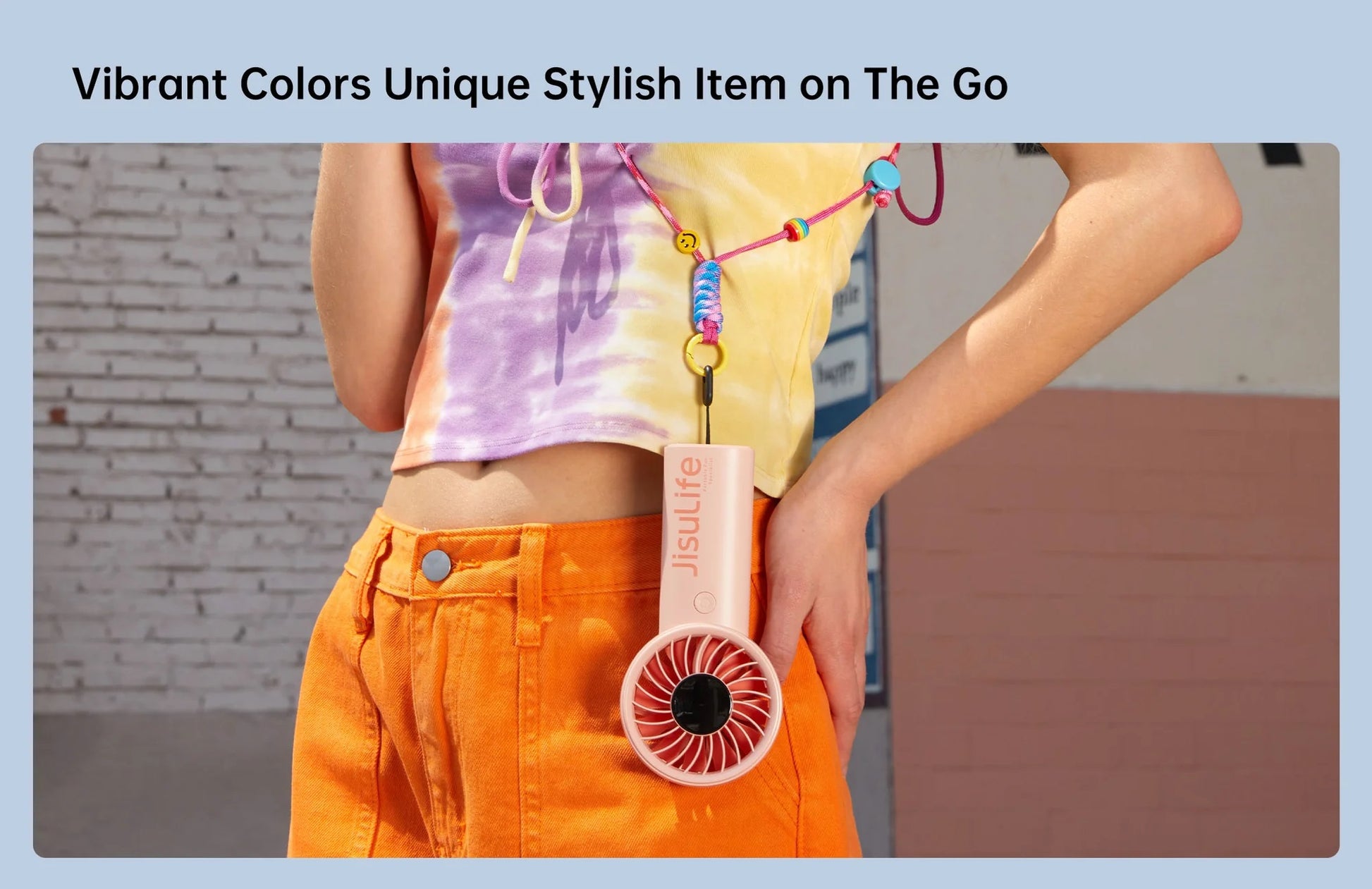 Jisulife life 4 strong wind fan handheld pink fan hanging from colorful lanyard worn with orange pants and tie dye shirt