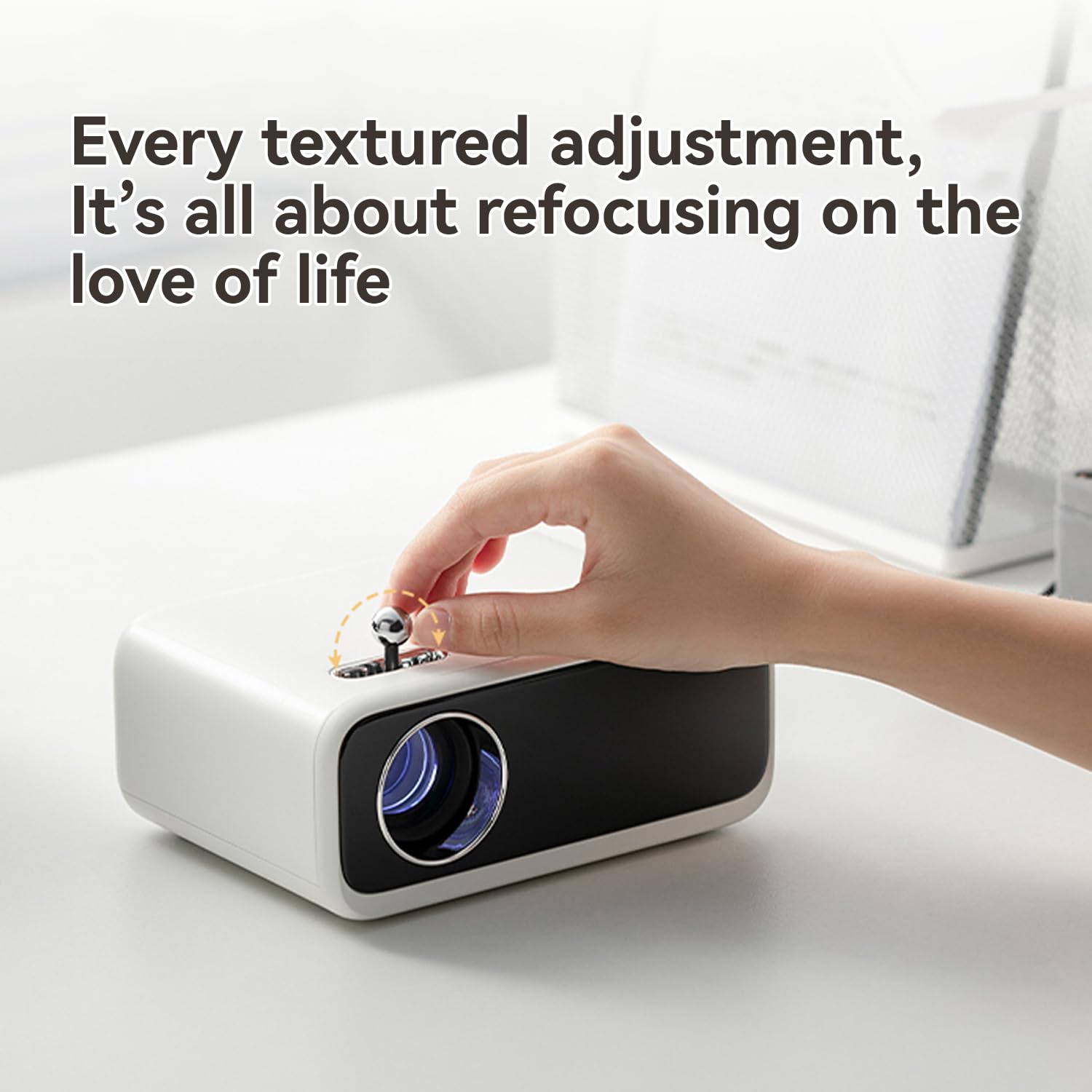 Hand adjusting focus knob on Wanbo Mini Pro smart projector on white table