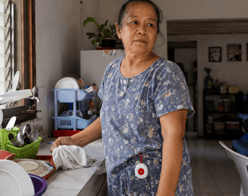 Elderly Filipino woman with Daytech waterproof caregiver SOS pager clipped to her waistband in a home kitchen