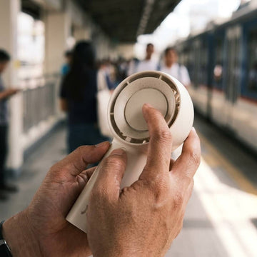 Hands troubleshooting a portable hand fan, JISULIFE FA43 checked on an MRT platform