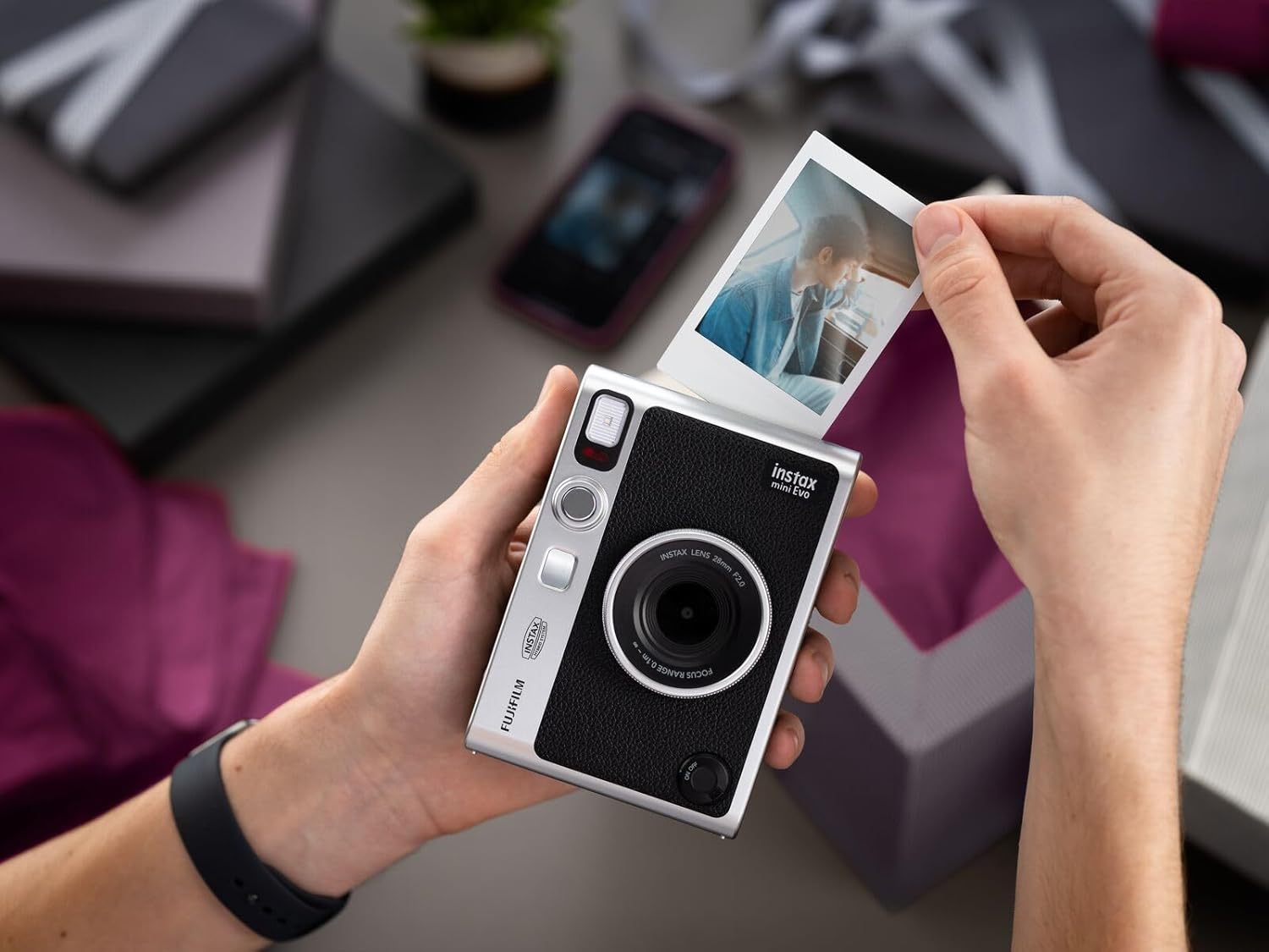 Person holding Mini Evo Hybrid Instant Film Camera with a printed photo in a festive setting
