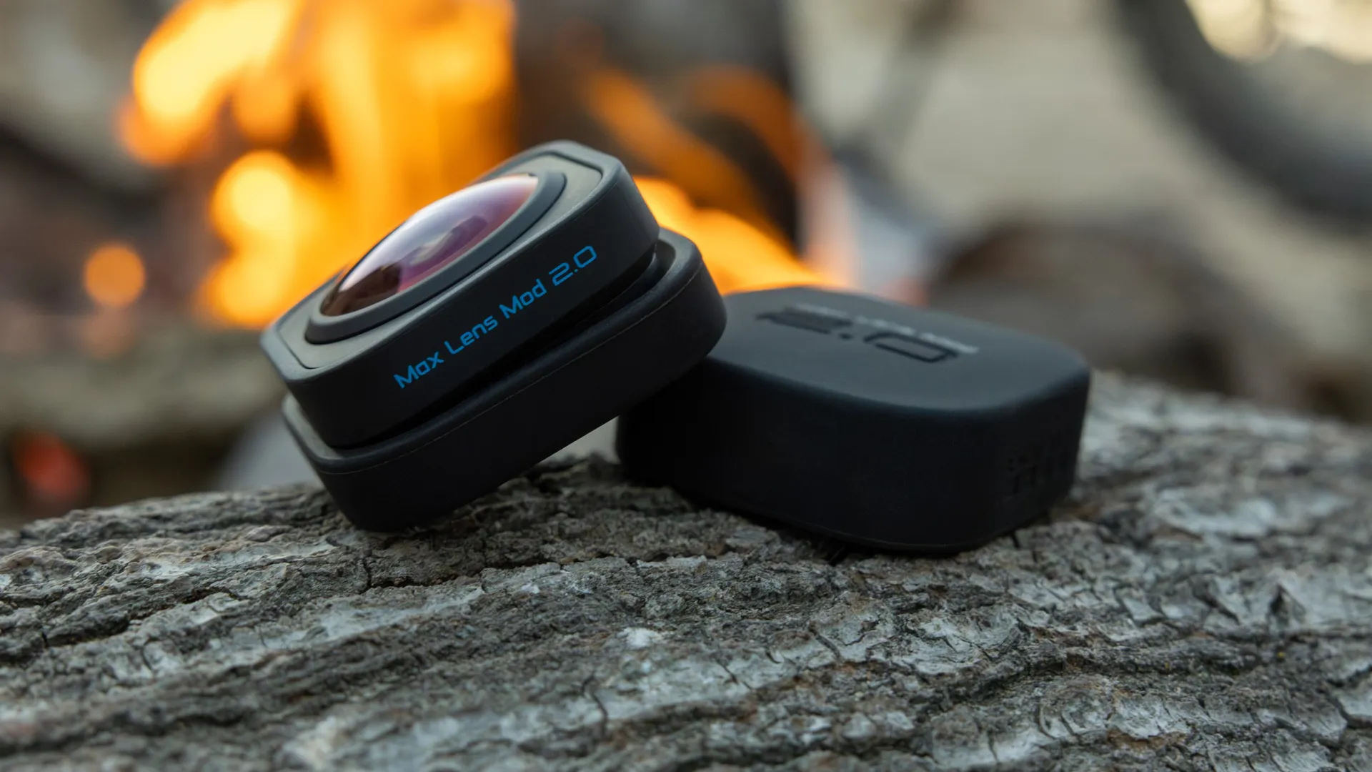 GoPro Max Lens Mod 2.0 camera lens accessory positioned on a log near a campfire