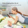 USB rechargeable desk fan in peach color on picnic blanket with woman using phone