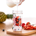 Pouring milk into a Portable Juicer Blender filled with fresh strawberries and blueberries on a wooden cutting board