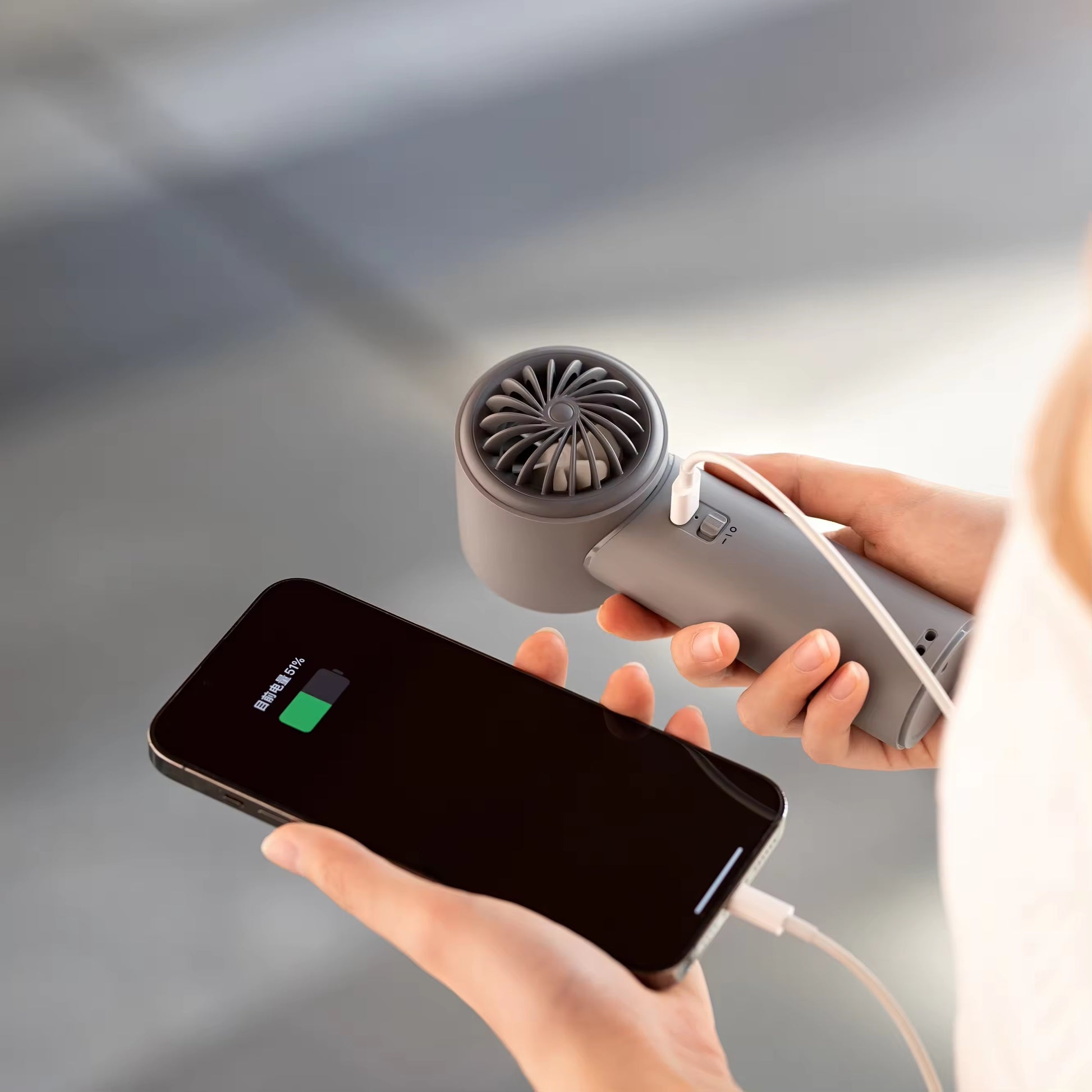 VMIDirect portable fan in hand, charging a smartphone for convenient cooling on the go