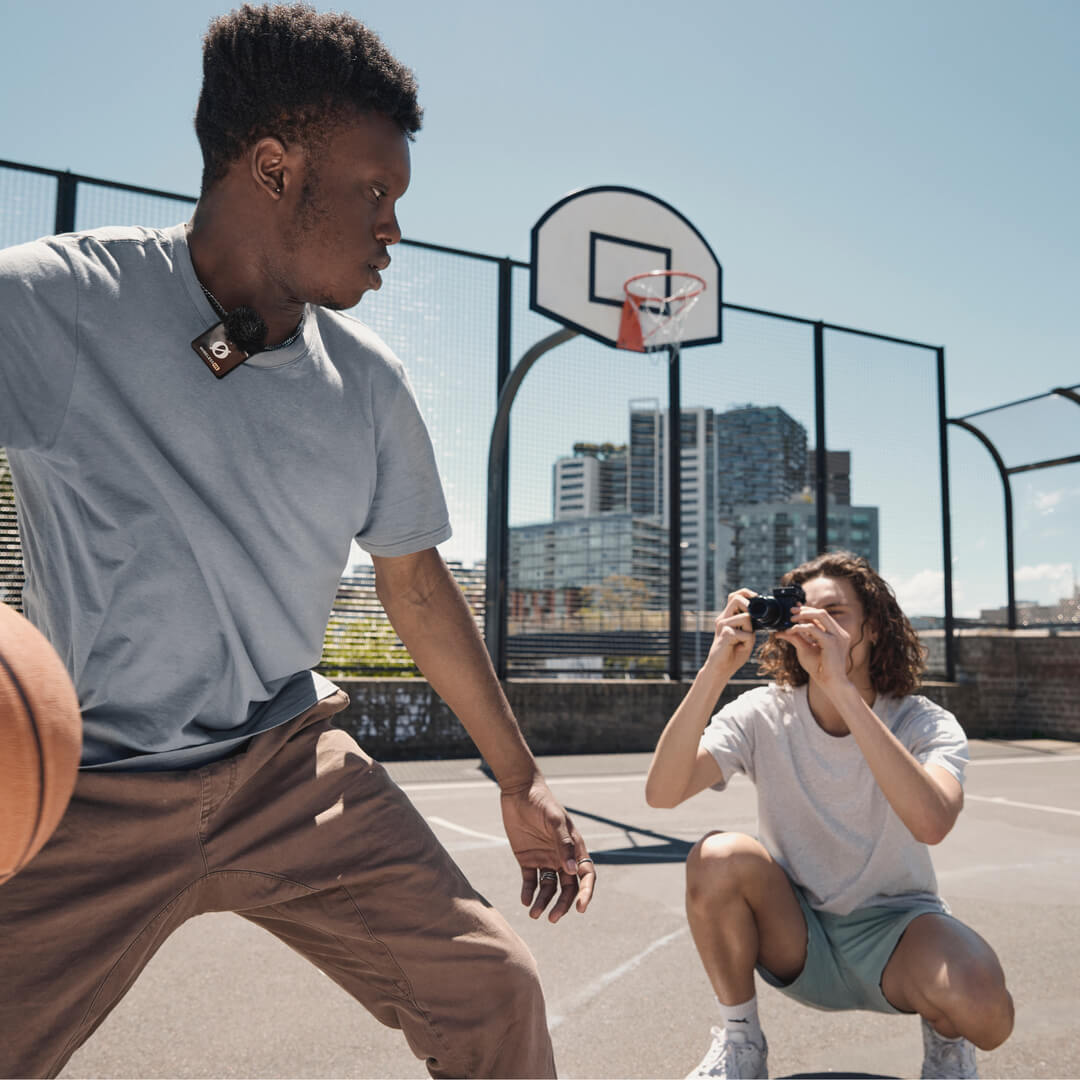 Young man playing basketball wearing a Rode Wireless ME Microphone System while a friend captures the moment