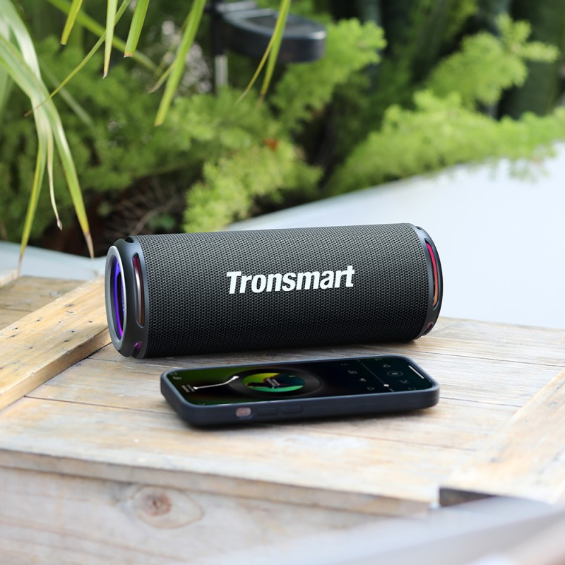 Tronsmart Portable Bluetooth Speaker on a wooden surface with a smartphone nearby, ideal for outdoor use