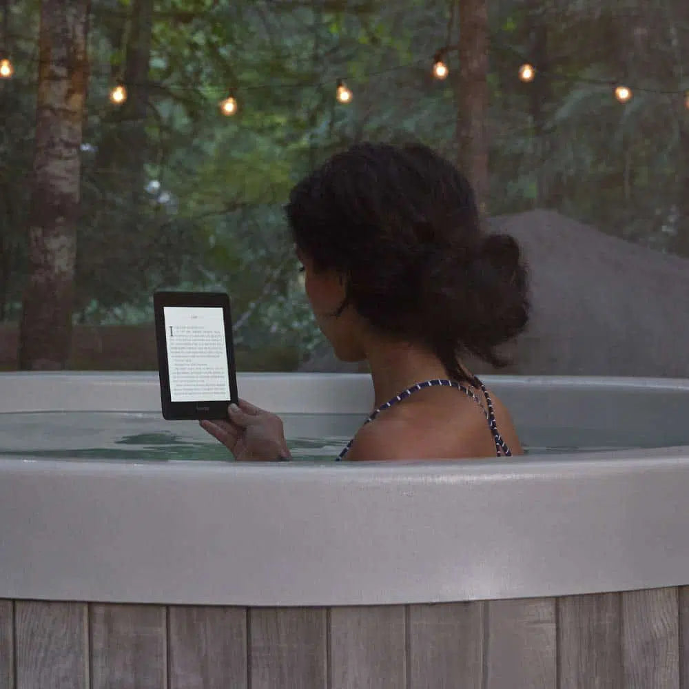 Person relaxing in a hot tub reading a Wireless E-Ink eReader in a serene outdoor setting