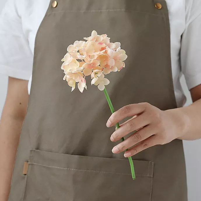 Person holding a delicate stem of artificial flowers silk in a neutral-toned apron for decoration