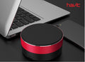 Havit Bluetooth Speaker in red, placed next to a laptop and smartphone for portable audio enjoyment