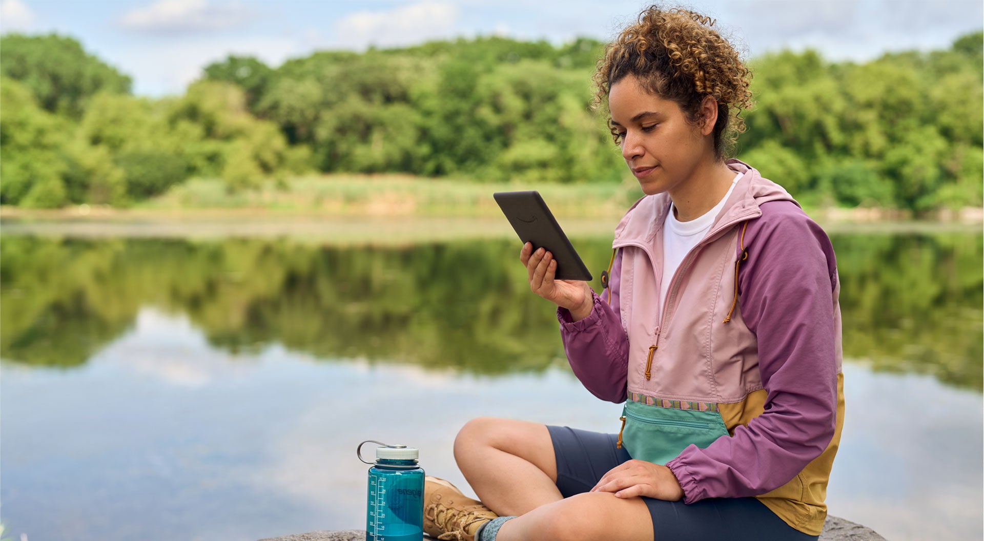 Person reading a VMIDirect Waterproof E-Reader by a serene lake on a sunny day