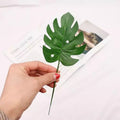 Hand holding a realistic simulation artificial green plant leaf for home decor or photography setups