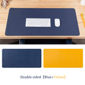 Double sided leather desk pad in blue and yellow with a keyboard and mouse on a wooden desk