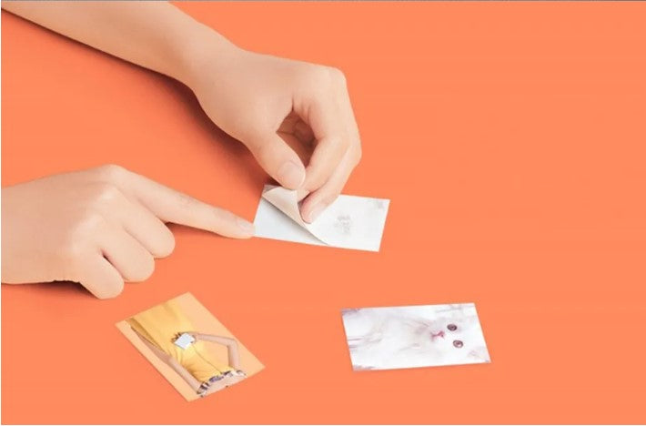 VMIDirect Pocket Photo Printer Paper being used to peel off a print from a hand on an orange background